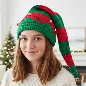 May include: A green and red striped crochet elf hat with gold bells. The hat has a long, pointed tip and is worn by a person. The hat is a festive accessory for Christmas or holiday celebrations.