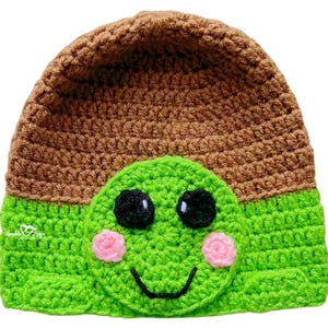 May include: A handmade crochet hat in brown and green, featuring a turtle design. The hat has a brown top and a green face with black eyes, pink cheeks, and a smiling mouth. A fun and whimsical accessory.