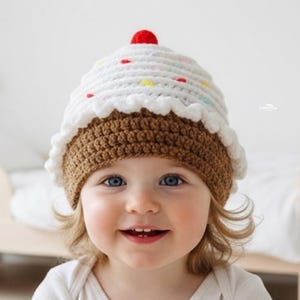 May include: A crocheted cupcake hat with a brown base, white frosting, and a red cherry on top. The hat has colorful sprinkles and a scalloped edge. This handmade hat is a fun accessory for babies and toddlers.