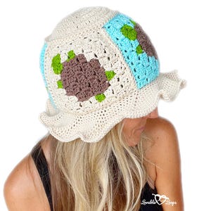 May include: A cream-colored, crocheted sun hat with a ruffled brim. The hat features square patches of turquoise, brown, and green, creating a patchwork design. The hat is handmade and has a unique, textured appearance.