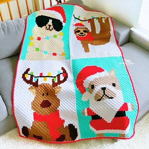 May include: A handmade Christmas-themed blanket featuring four squares with festive animal designs. The blanket showcases a llama with sunglasses, a sloth, a reindeer, and a dog, all wearing Santa hats and holiday lights. The blanket is white, red, and turquoise.