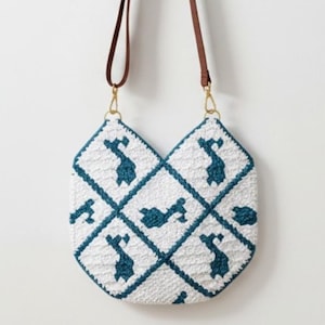 Puede incluir: Bolso de mano blanco y verde azulado con estampado geométrico y correa marrón. El bolso presenta una forma única y un diseño repetitivo de formas verde azulado sobre un fondo blanco. La correa es de material marrón similar al cuero.
