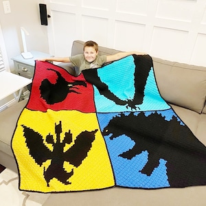 May include: A handmade, colorful crochet blanket featuring four distinct sections. Each section showcases a black silhouette of a monster against a background of red, blue, yellow, and turquoise. The blanket is displayed on a gray couch.