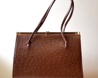 May include: A vintage brown handbag with a textured surface and two long handles. The rectangular bag has a gold-colored clasp and trim. The bag is a medium size, suitable for carrying essentials.