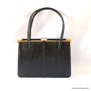 May include: A black vintage handbag with a textured, reptile-like pattern. The rectangular purse has a gold-toned clasp and trim, with two matching handles. The bag is a classic style, suitable for various occasions.