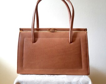 May include: A vintage, rectangular handbag in a warm, tan color. The bag features a structured design with a stitched border, a gold-toned clasp, and matching handles. The bag is approximately 12 inches wide and 8 inches tall.