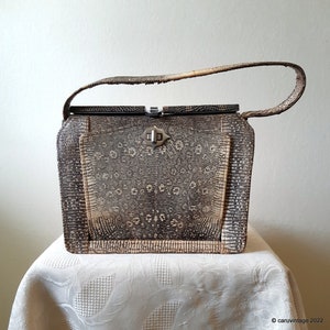 May include: A vintage handbag made of brown snakeskin with a silver clasp. The bag has a top handle and a flap closure.