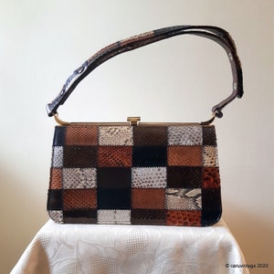 May include: A vintage handbag with a patchwork design. The rectangular bag features a variety of brown, black, and white snake skin squares. It has a gold-tone clasp and a matching snakeskin handle.