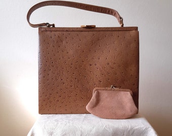 May include: A vintage brown handbag with a matching small coin purse. The handbag has a structured, square shape with a handle and clasp closure. The textured surface of the bag and purse suggests an ostrich leather design. The coin purse is a light pink color.