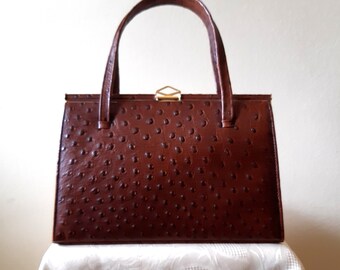 May include: A vintage brown handbag with a textured surface and a rectangular shape. The bag features a top handle, a gold-colored clasp, and a structured design. The bag is sitting on a white surface.