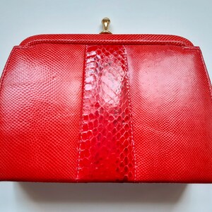 May include: A vibrant red vintage handbag with a reptile-like texture. The rectangular bag has a central panel with a contrasting scale pattern and a gold-coloured clasp.