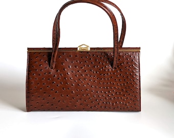 May include: A vintage brown handbag with a textured surface and two curved handles. The rectangular bag features a gold-colored clasp and trim. The bag's color is a rich, warm brown.