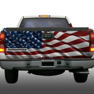 May include: A silver pickup truck with a red, white, and blue American flag design on the tailgate. The truck has a black bumper and black wheels.