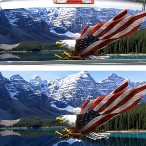 May include: A bald eagle with outstretched wings holding an American flag flies over a mountain lake with snow-capped peaks in the background.