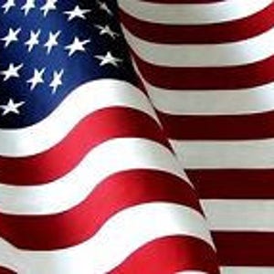May include: A close-up of a waving American flag with red and white stripes and blue stars. The flag is made of fabric and is waving in the wind.
