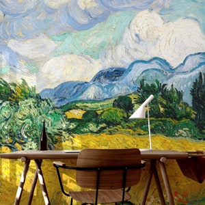 May include: A wooden desk with a white lamp and a chair in front of a wall with a painting of a landscape with blue sky and yellow fields.