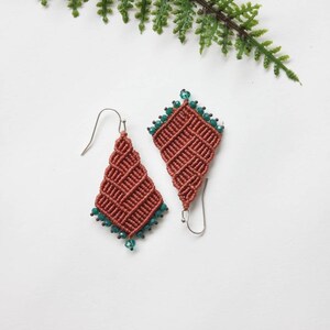 May include: A pair of terracotta-coloured knotted earrings with teal crystal accents. The earrings are in the shape of a diamond and have a silver hook.