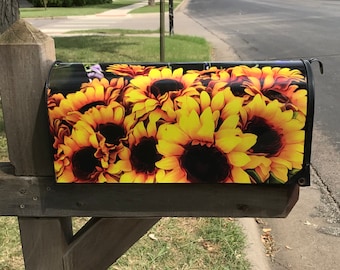 Könnte beinhalten: Ein schwarzer Briefkasten mit einem bunten Sonnenblumenmuster. Der Briefkasten ist an einem Holzpfosten befestigt.