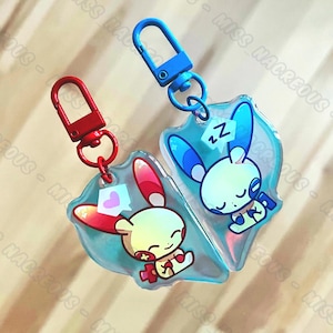 May include: Two blue and pink keychains with cartoon characters. The keychain on the left features a pink character with a heart and the keychain on the right features a blue character with a Z.