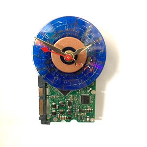 May include: A clock made from a recycled computer hard drive and a blue vinyl record. The clock face is a copper circle with gold hands and a red second hand.