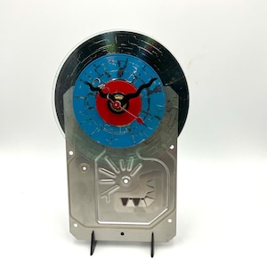 May include: A clock made from a repurposed computer hard drive with a blue and red face and black hands.
