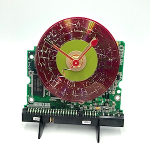 May include: A clock made from a repurposed computer hard drive with a red and green face. The clock hands are made from metal and the clock face is a CD.