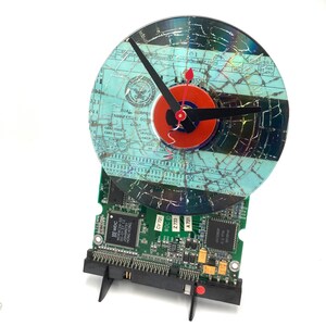 May include: A clock made from a repurposed computer hard drive and a cracked CD. The clock face is a blue and white document with the text "Dual Erpos Engineering Dept. Card Code Upper Lower" and "101 Card Class". The clock hands are black and red.