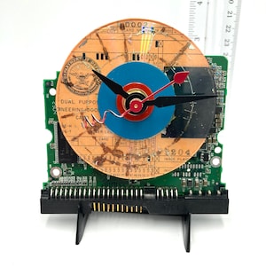 May include: A clock made from a repurposed computer hard drive with a blue, red and orange face. The clock face is made from a vintage government document with the text "Dual Purpose Engineering Document Card No. 204".