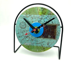 May include: A clock made from a recycled CD with a blue and green face and black hands. The clock is on a black metal stand.