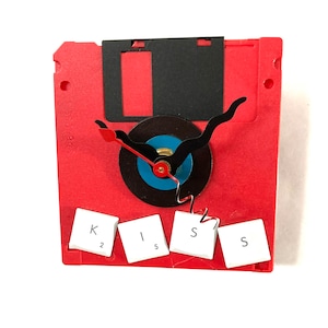 May include: Red floppy disk clock with a black vinyl record face and black hands. The clock is decorated with four white keys from a keyboard spelling out "KISS".