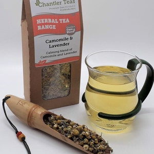 Puede incluir: Una caja de papel marr&oacute;n con una etiqueta blanca que dice "Chantler Teas Herbal Tea Range Camomile & Lavender Calming blend of Camomile and Lavender". La caja contiene flores secas de manzanilla y lavanda. Una taza de t&eacute; de vidrio est&aacute; al lado de la caja. Una cuchara de madera con flores secas de manzanilla y lavanda est&aacute; en primer plano.