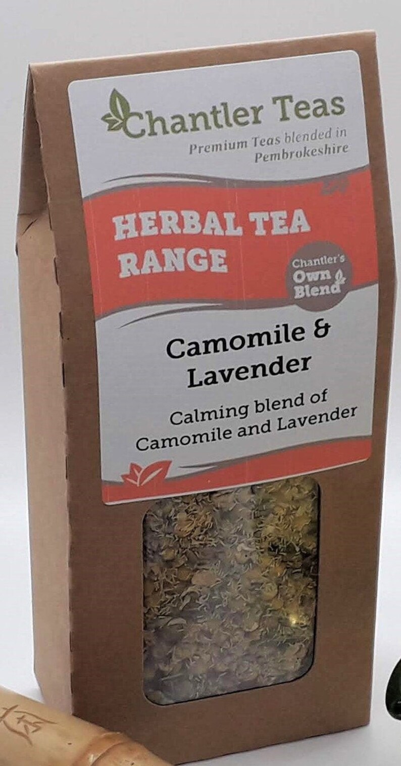 Puede incluir: Una caja de cart&oacute;n marr&oacute;n con una ventana que muestra una mezcla de flores secas de manzanilla y lavanda. La caja est&aacute; etiquetada "Chantler Teas Herbal Tea Range Camomile & Lavender Calming blend of Camomile and Lavender".