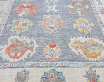 May include: A gray rug with a colorful floral pattern. The rug has a light blue border with a white inner border.