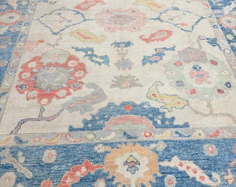 May include: A vintage rug with a cream background and a blue, red, and yellow floral pattern. The rug has a border with a blue background and a white and yellow floral pattern.