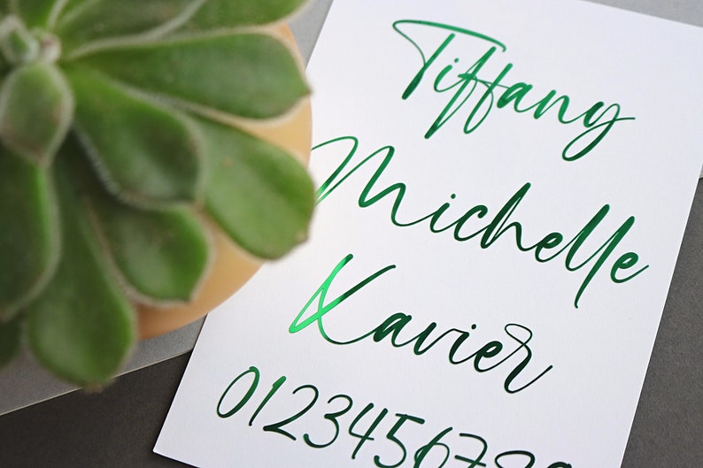 May include: A white card with the names Tiffany, Michelle, and Xavier written in green cursive script. The numbers 012345678 are also written in green cursive script.