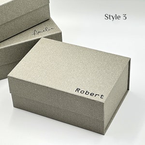 Puede incluir: Una caja de regalo gris con una superficie texturizada y el nombre "Robert" impreso en la parte delantera. La caja está cerrada y tiene un cierre magnético. Estilo 3.