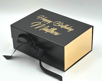 May include: Black gift box with a gold lid and a black ribbon. The box has the text "Happy Birthday Matthew" written in gold lettering.