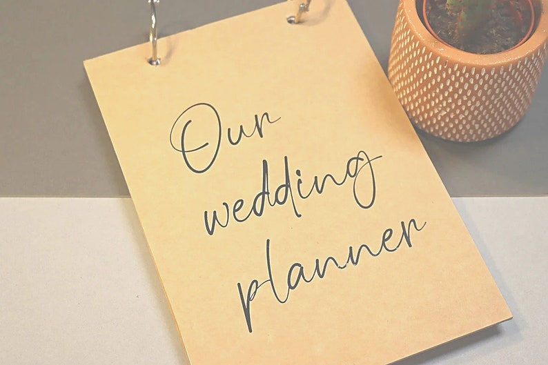 May include: A brown paper wedding planner with a silver ring binder and the text "Our wedding planner" written in black cursive.