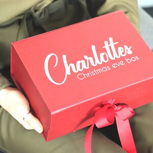 May include: A red gift box with a white ribbon and the text "Charlotte's Christmas Eve Box" printed on the top.