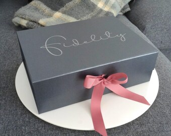 May include: A dark gray gift box with the word "Fidelity" printed in white on the top. The box is tied with a pink ribbon.