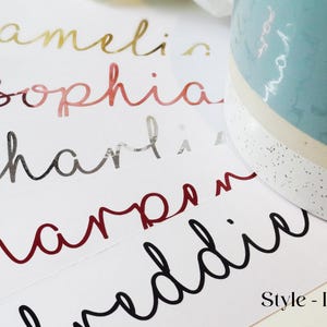 Puede incluir: Una superficie blanca con cinco nombres escritos en diferentes colores y fuentes: Amelia en dorado, Sophia en rosa, Charli en plateado, Harper en rojo y Maddie en negro. El texto "Style - Ilov" está en la parte inferior de la imagen.