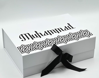 May include: White gift box with a black ribbon and a black and white geometric design. The box is labeled "Muhammad".
