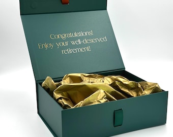 May include: A green gift box with a gold ribbon and a gold inscription that reads "Congratulations! Enjoy your well-deserved retirement!" The box is open and lined with gold tissue paper.