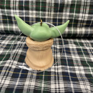 Peut inclure: Une d&eacute;coration de No&euml;l verte et marron en forme de personnage de la franchise Star Wars. La d&eacute;coration a une boucle de ficelle pour l'accrocher.