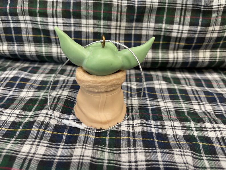 Peut inclure: Une d&eacute;coration de No&euml;l verte et marron en forme de personnage de la franchise Star Wars. La d&eacute;coration a une boucle de ficelle pour l'accrocher.