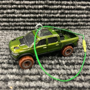 May include: Green toy truck with a black grill and black wheels. The truck has a green string attached to it.
