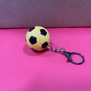 May include: A yellow and black soccer ball keychain with a silver metal key ring.