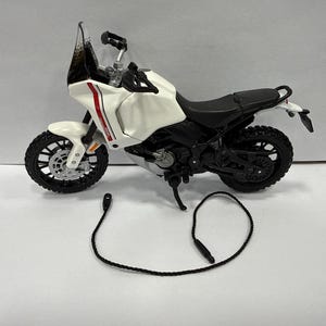Könnte beinhalten: Ein weißes und schwarzes Spielzeugmotorrad mit schwarzem Sitz, Rädern und einer durchsichtigen Windschutzscheibe. Das Motorrad hat rote und weiße Akzente und ein schwarzes Kabel. Es ist ein Spielzeug.