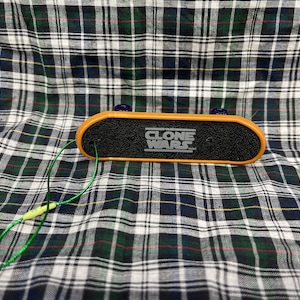 May include: A brown and black fingerboard with a green string attached. The fingerboard has the words "Clone Wars" printed on it.