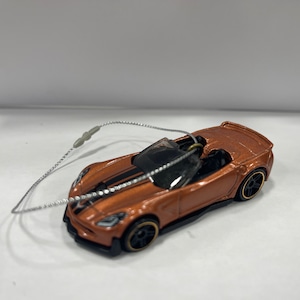 May include: A brown and black toy car with a black stripe down the hood. The car is a convertible and has a silver string attached to it.